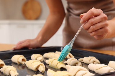 Photo of Woman brushing egg wash onto raw croissants at table indoors, closeup