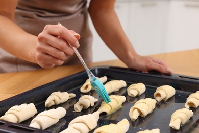 Photo of Woman brushing egg wash onto raw croissants at table indoors, closeup