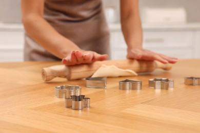 Photo of Woman rolling dough for cookies at wooden table indoors, closeup