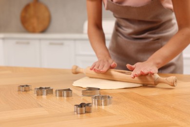 Photo of Woman rolling dough for cookies at wooden table indoors, closeup. Space for text