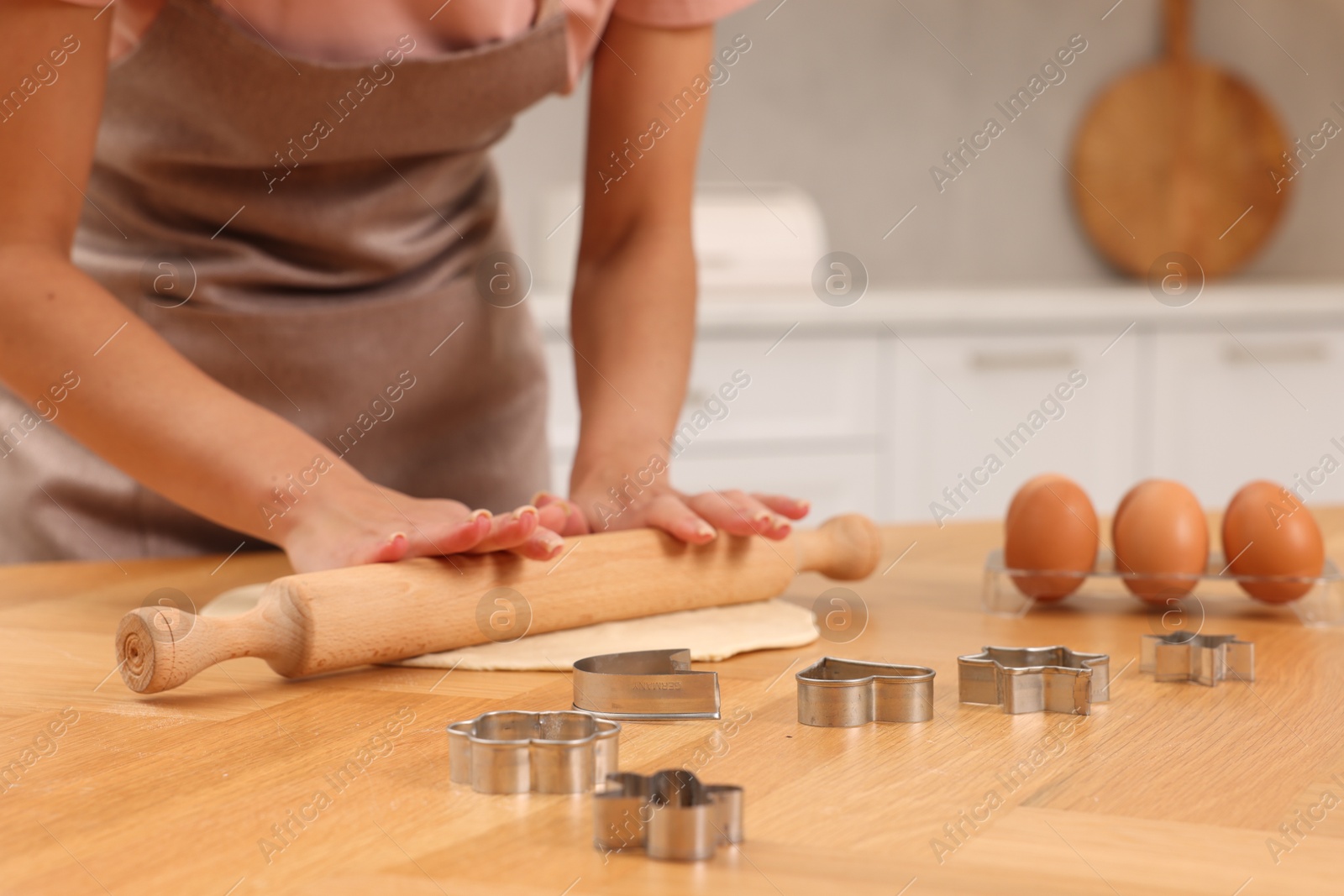 Photo of Woman rolling dough for cookies at wooden table indoors, closeup