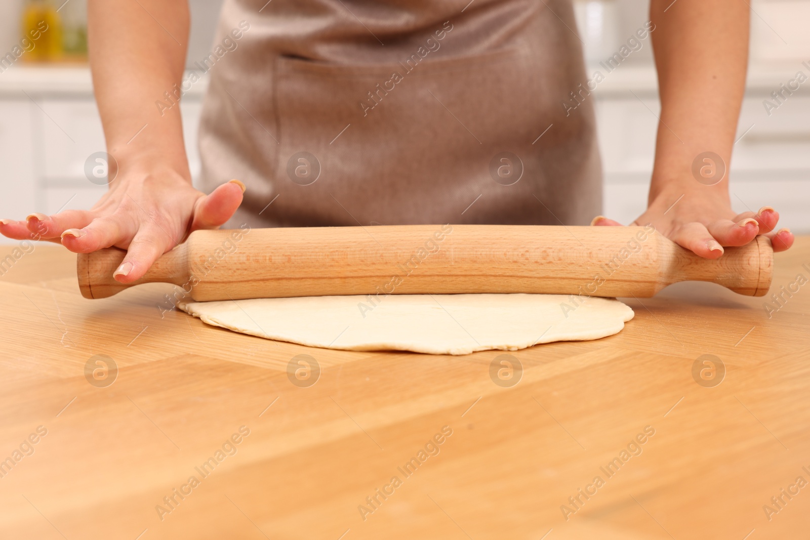 Photo of Woman rolling dough at wooden table indoors, closeup