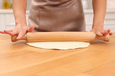 Woman rolling dough at wooden table indoors, closeup