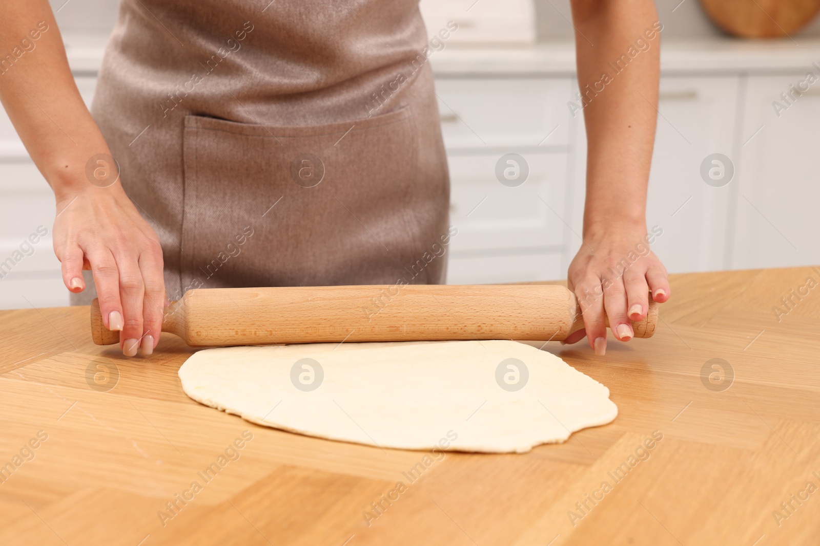 Photo of Woman rolling dough at wooden table indoors, closeup