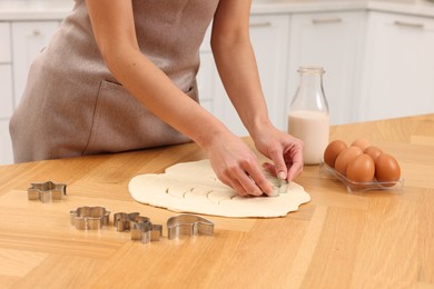 Photo of Woman cutting out cookies at wooden table indoors, closeup