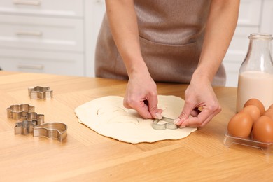 Woman cutting out cookies at wooden table indoors, closeup