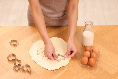 Woman cutting out cookies at wooden table indoors, closeup