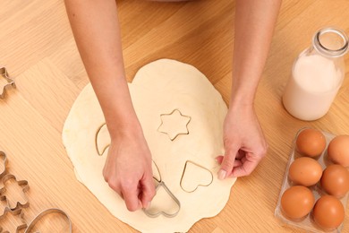 Photo of Woman cutting out cookies at wooden table indoors, top view