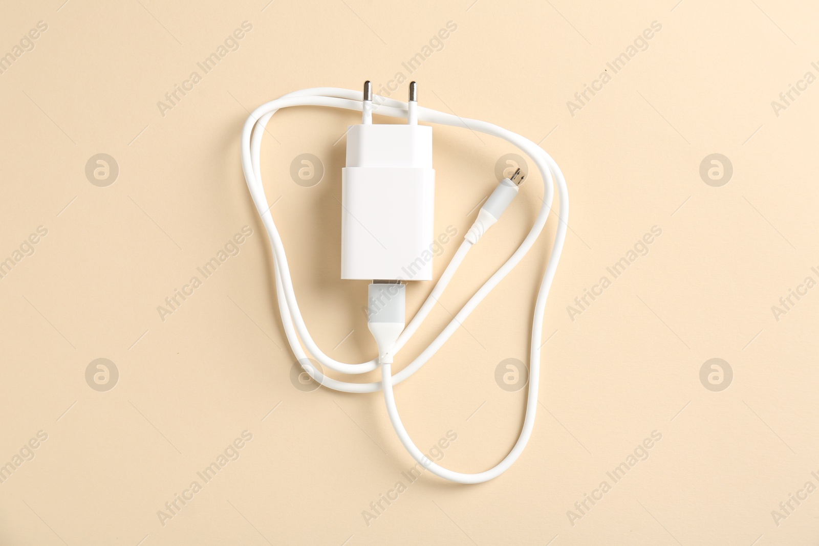 Photo of USB power adapter with charge cable on beige background, top view