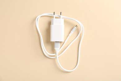 Photo of USB power adapter with charge cable on beige background, top view