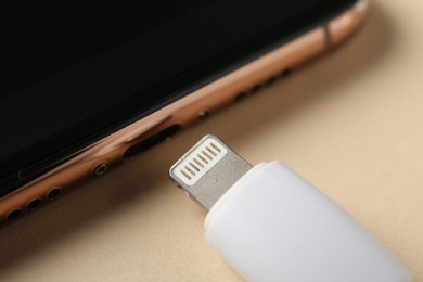 Photo of USB charge cable and smartphone on beige background, closeup