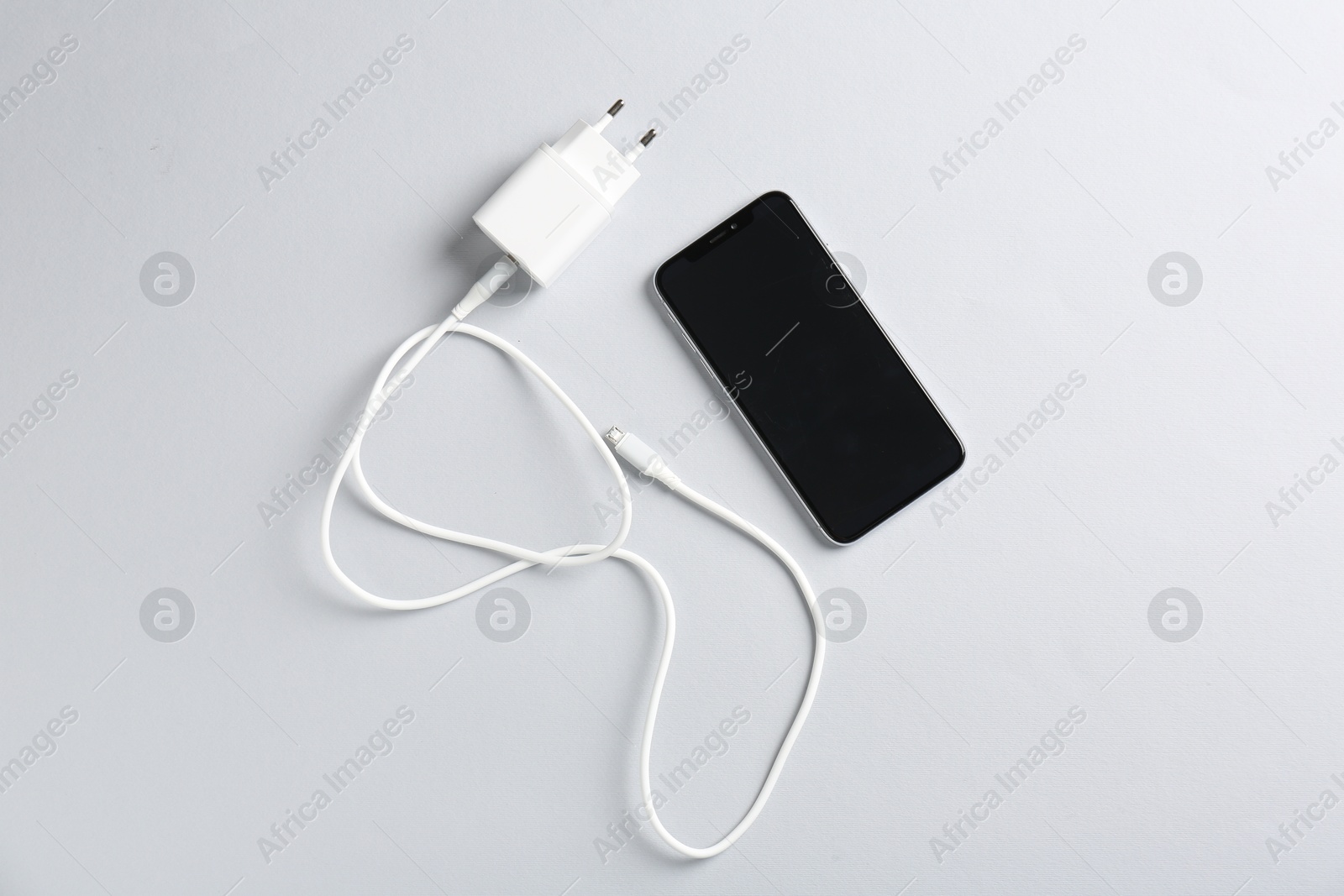 Photo of USB power adapter with charge cable and smartphone on white background, flat lay