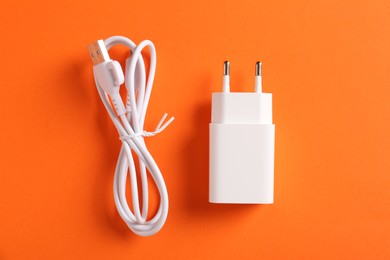 Photo of USB power adapter and charge cable on orange background, flat lay