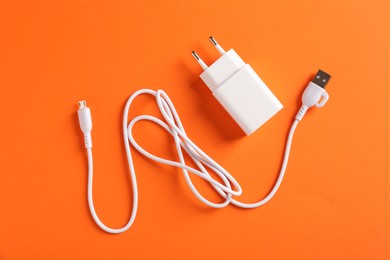 Photo of Charging adapter and USB cable on orange background, flat lay