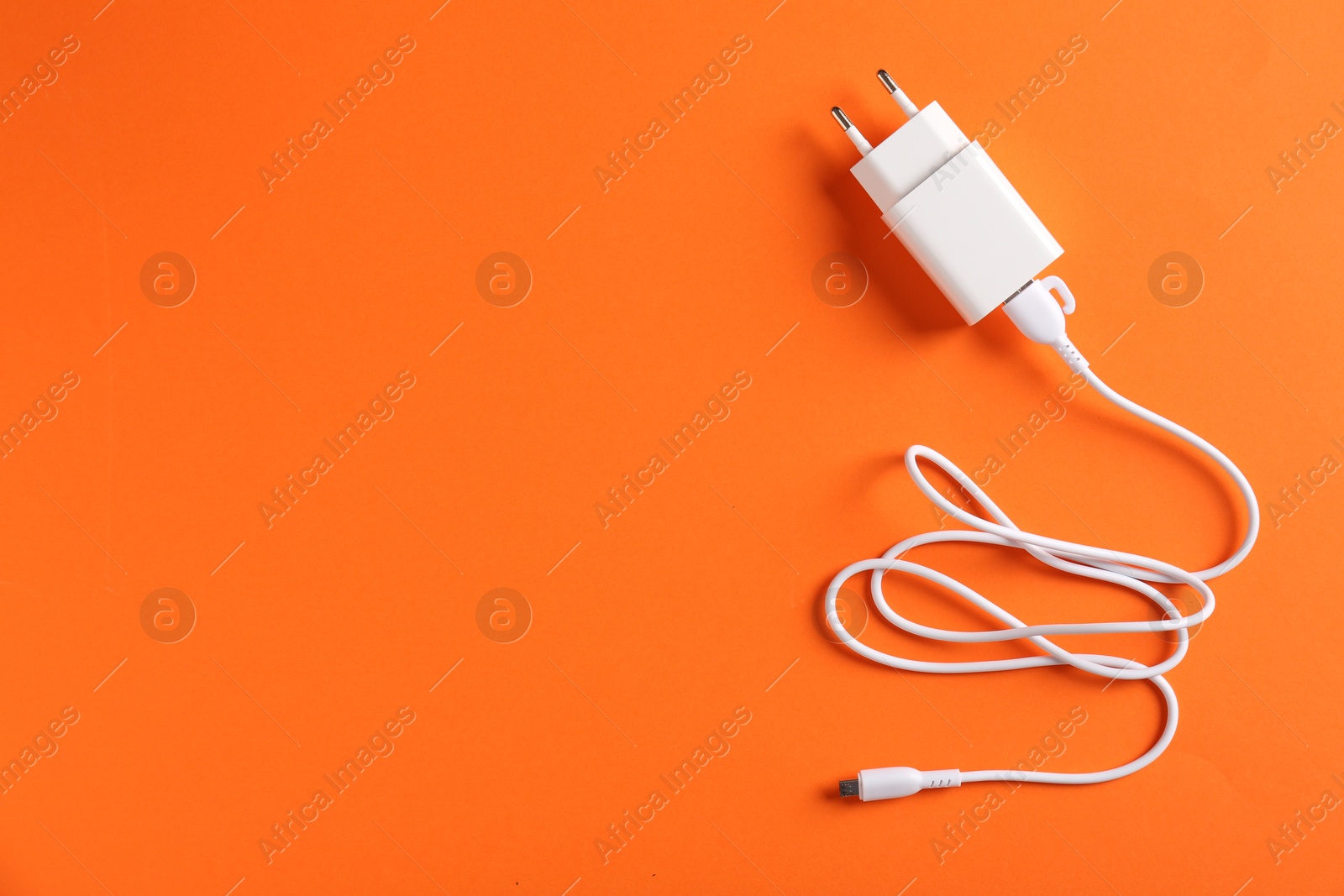 Photo of USB power adapter with charge cable on orange background, top view. Space for text