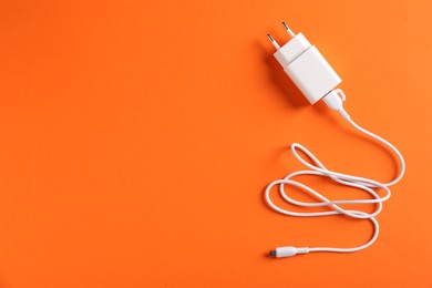 Photo of USB power adapter with charge cable on orange background, top view. Space for text