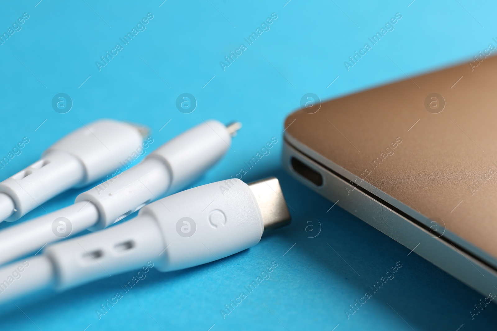 Photo of USB charge cables and laptop on light blue background, closeup