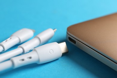 Photo of USB charge cables and laptop on light blue background, closeup