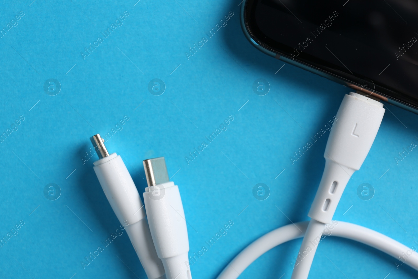 Photo of USB charge cable connected to smartphone on light blue background, top view