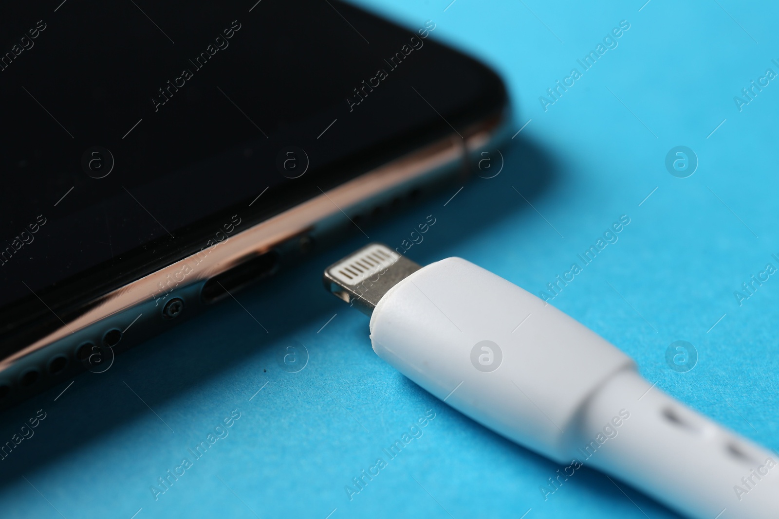 Photo of USB charge cable with lightning connector and smartphone on light blue background, closeup