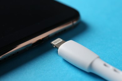 Photo of USB charge cable with lightning connector and smartphone on light blue background, closeup