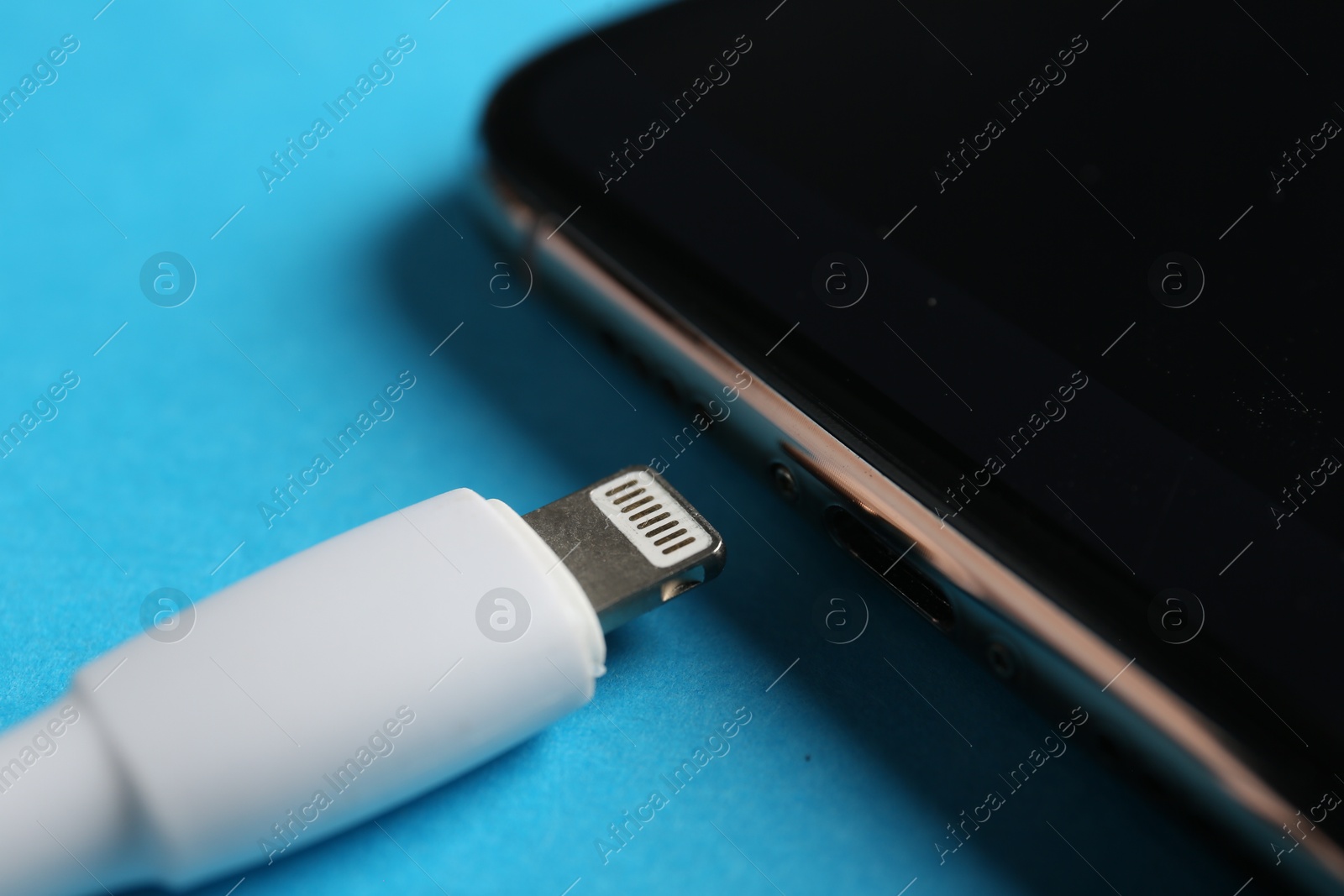 Photo of USB charge cable with lightning connector and smartphone on light blue background, closeup