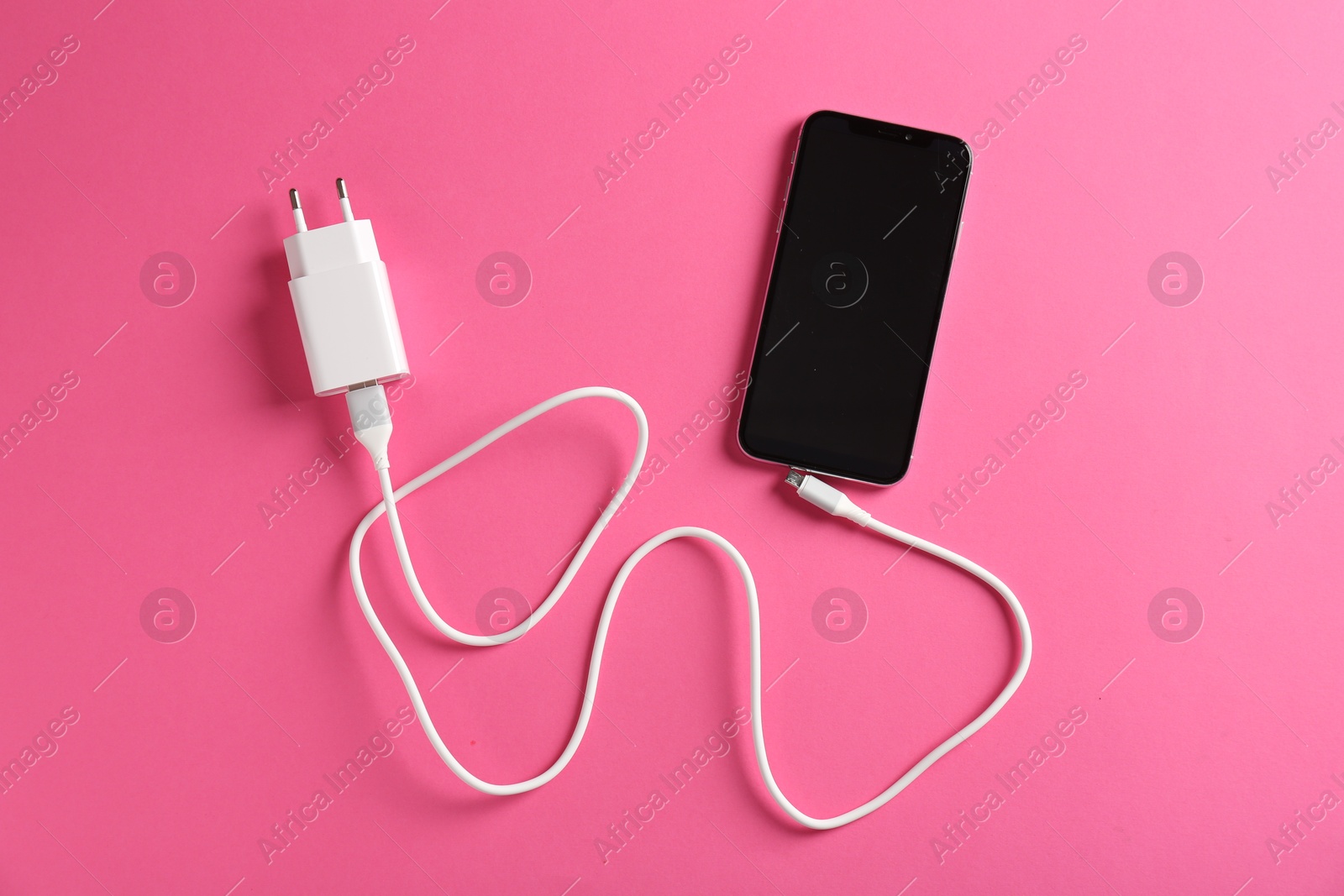 Photo of USB power adapter with charge cable and smartphone on pink background, flat lay