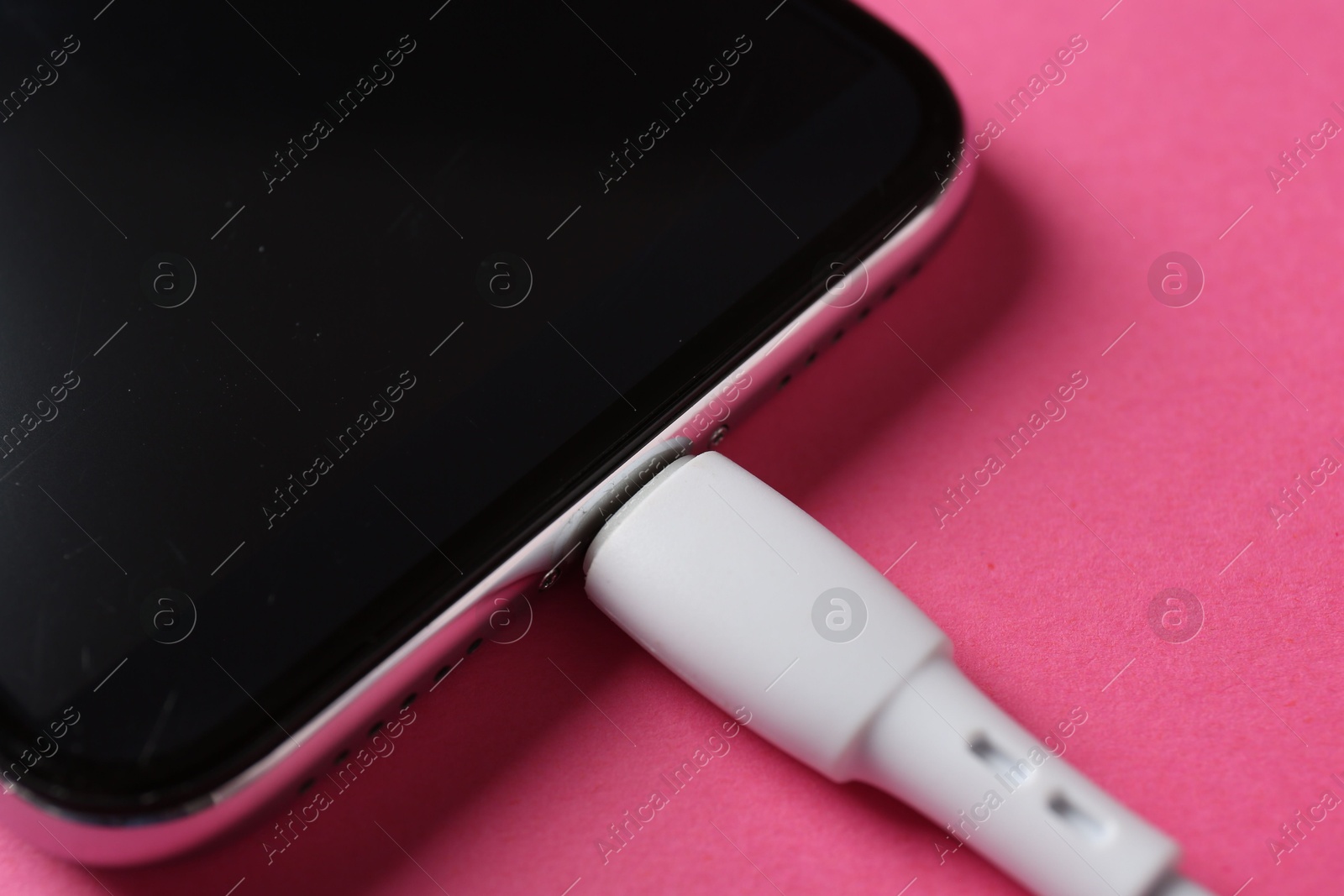 Photo of USB charge cable connected to smartphone on pink background, closeup