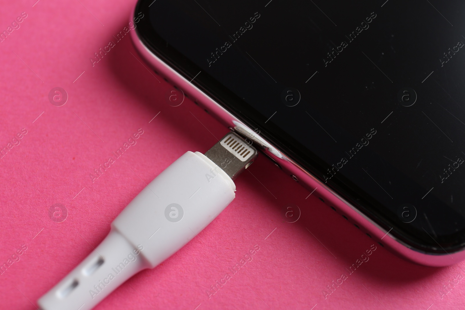 Photo of USB charge cable and smartphone on pink background, closeup