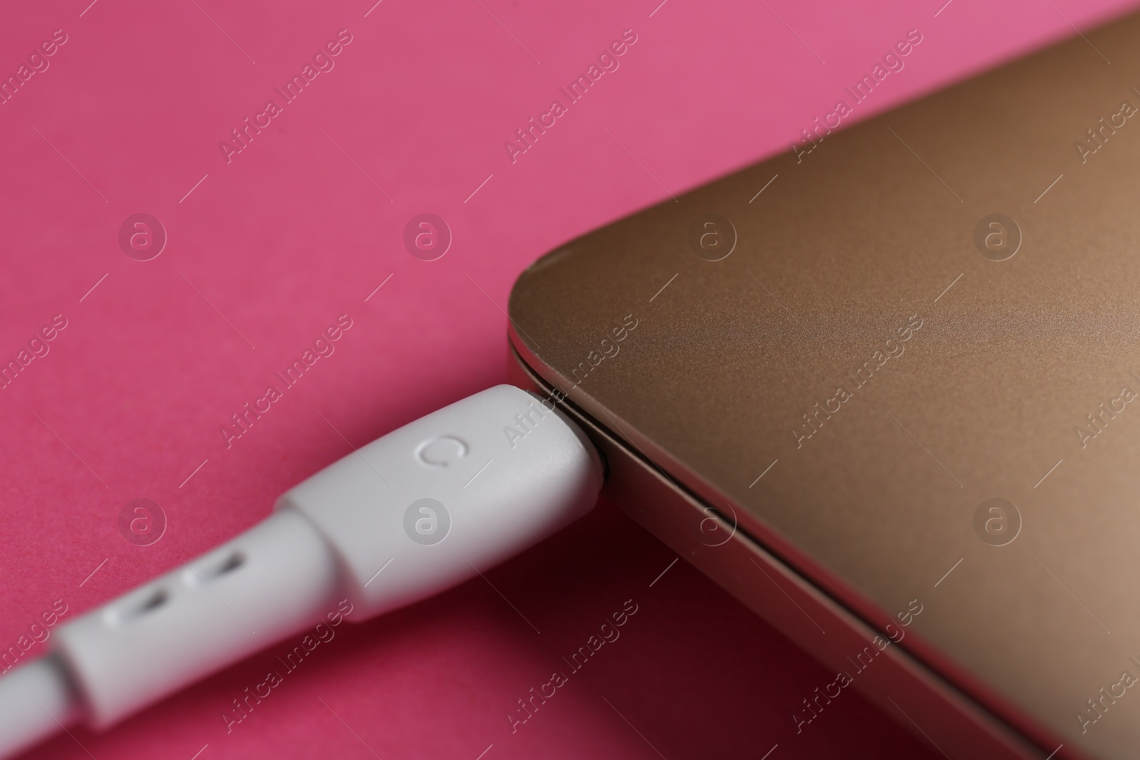 Photo of USB charge cable connected to laptop on pink background, closeup