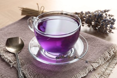 Photo of Aromatic lavender tea in glass cup, spoon and bunch of dry glowers on table, closeup