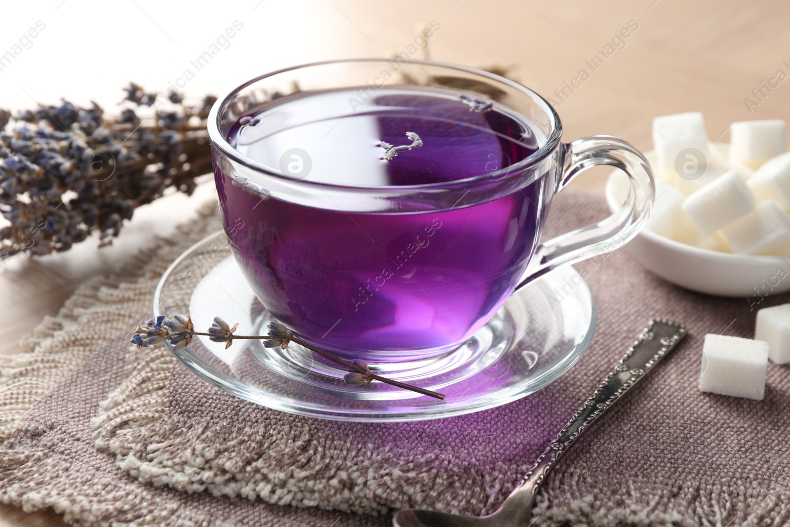 Photo of Aromatic lavender tea in glass cup, spoon and sugar cubes on table, closeup