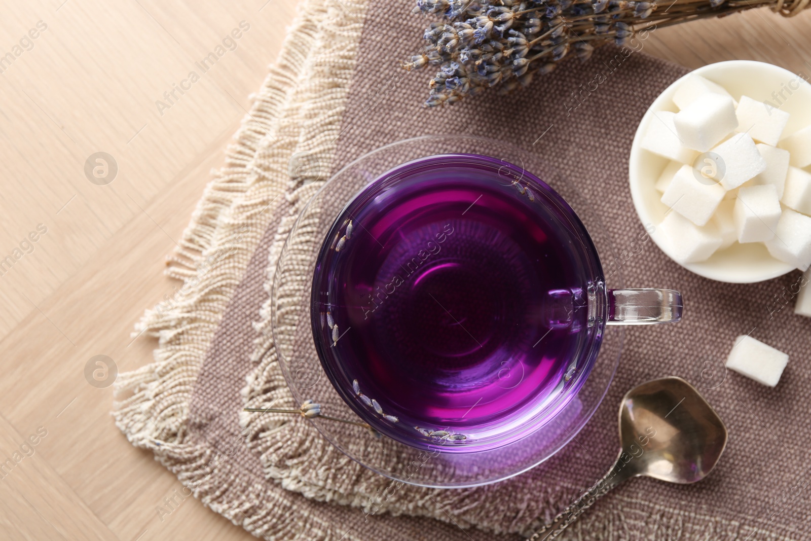 Photo of Aromatic lavender tea in glass cup, spoon, sugar cubes and dry flowers on wooden table, top view. Space for text