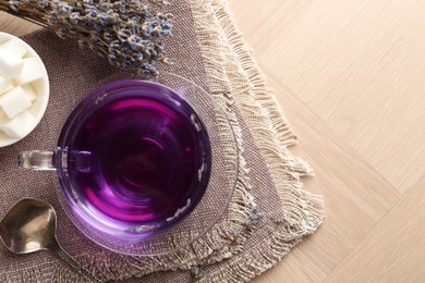 Aromatic lavender tea in glass cup, spoon, sugar cubes and dry flowers on wooden table, top view. Space for text