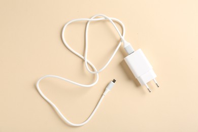 Photo of USB power adapter with charge cable on beige background, top view