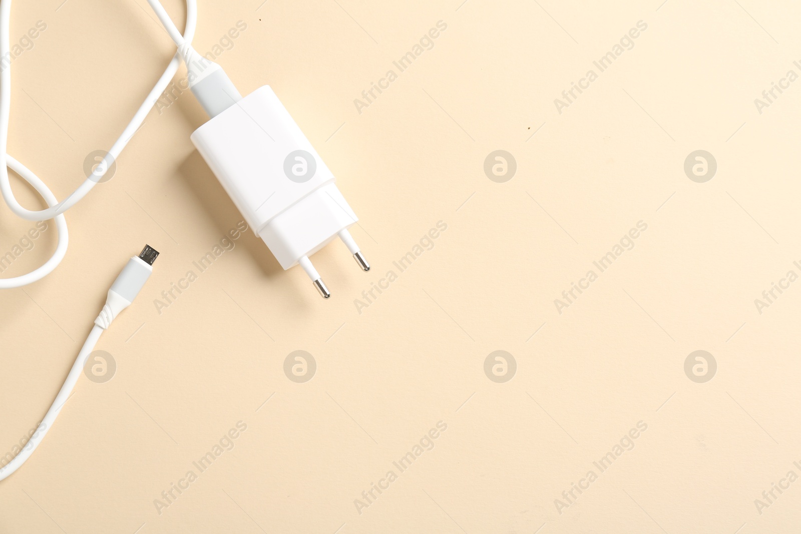 Photo of USB power adapter with charge cable on beige background, top view. Space for text