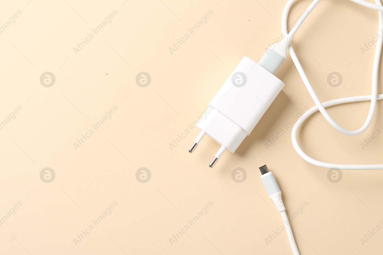 Photo of USB power adapter with charge cable on beige background, top view. Space for text