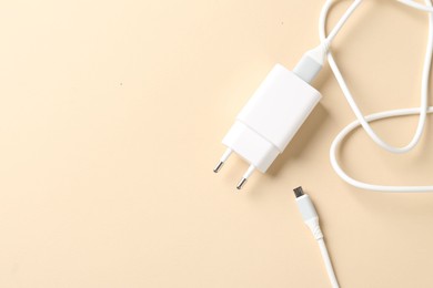 Photo of USB power adapter with charge cable on beige background, top view. Space for text