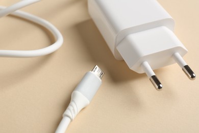 Photo of USB power adapter with charge cable on beige background, closeup