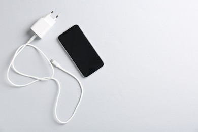 Photo of USB power adapter with charge cable and smartphone on white background, flat lay. Space for text