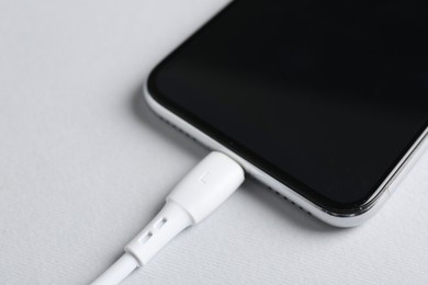 Photo of USB charge cable connected to smartphone on white background, closeup