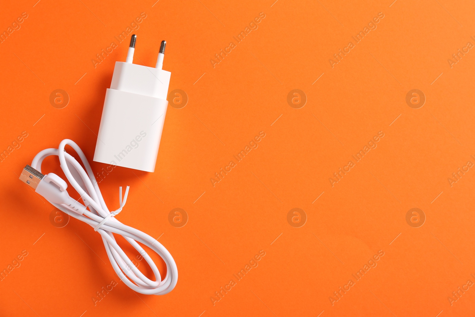 Photo of USB power adapter and charge cable on orange background, flat lay. Space for text