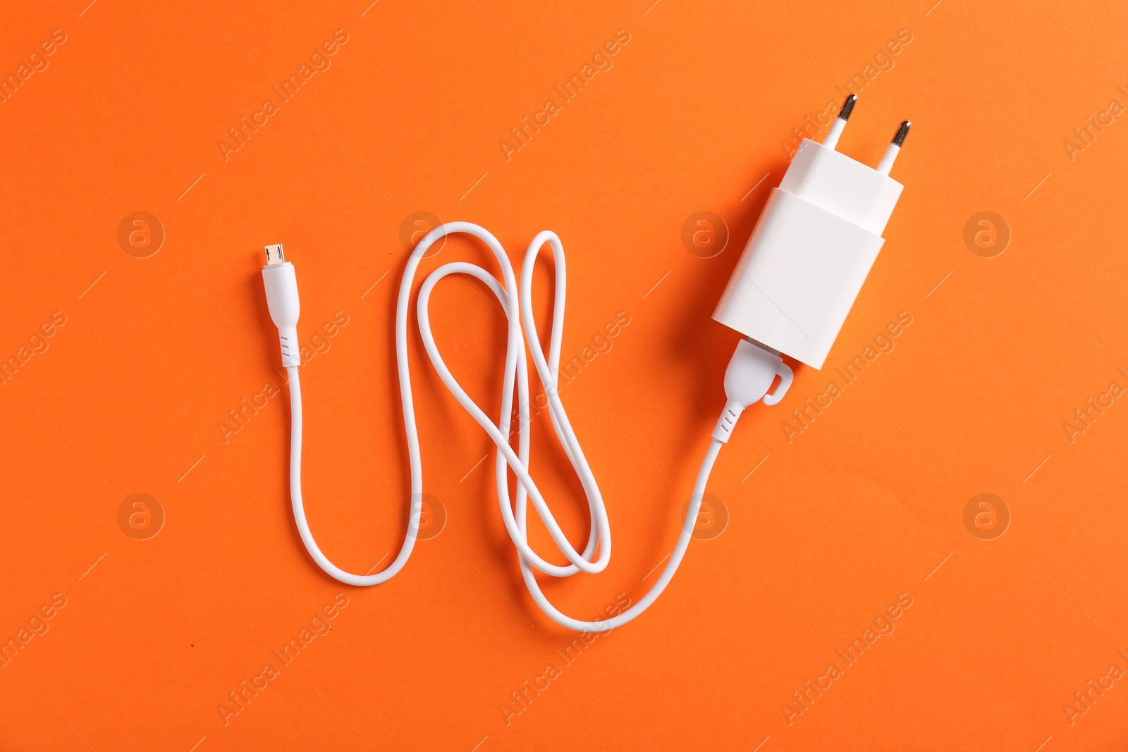 Photo of USB power adapter with charge cable on orange background, top view