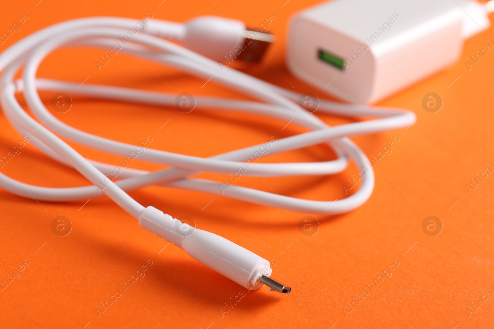 Photo of USB power adapter with charge cable on orange background, closeup