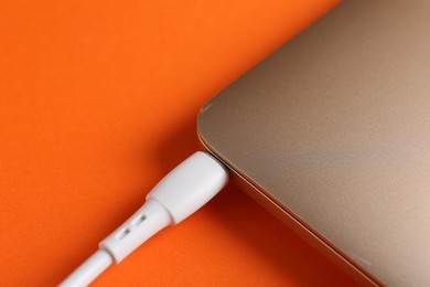 Photo of USB charge cable connected to laptop on orange background, closeup