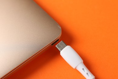 Photo of USB charge cable with laptop on orange background, closeup. Space for text