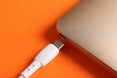 Photo of USB charge cable with lightning connector and laptop on orange background, closeup