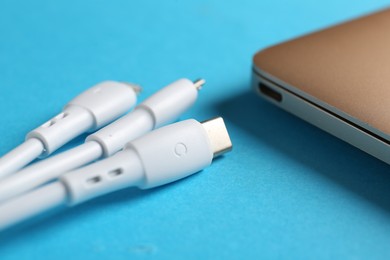 Photo of USB charge cables and laptop on light blue background, closeup