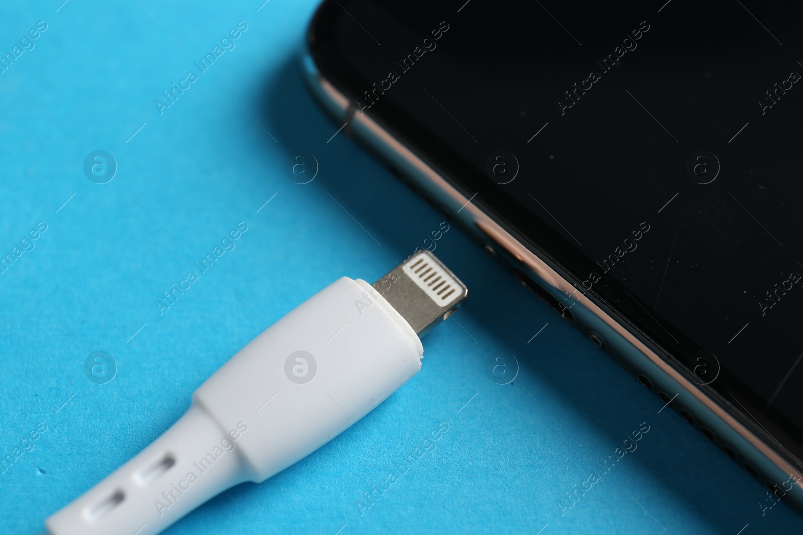 Photo of USB charge cable with lightning connector and smartphone on light blue background, closeup