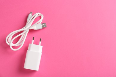 Photo of USB power adapter and charge cable on pink background, flat lay. Space for text